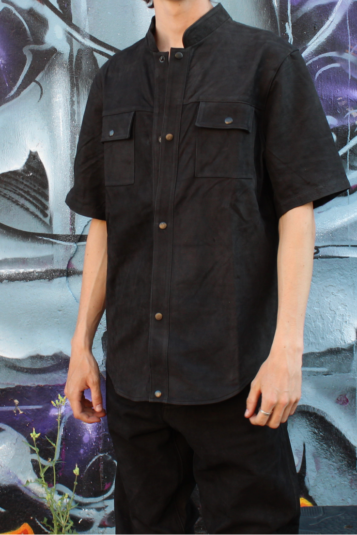 Person wearing a custom black leather outfit standing in front of a colorful graffiti wall.