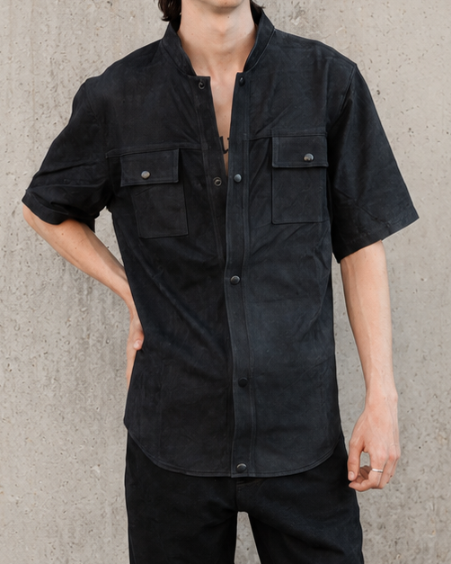 Person wearing a handmade black leather shirt and pants with a cap against a concrete wall.
