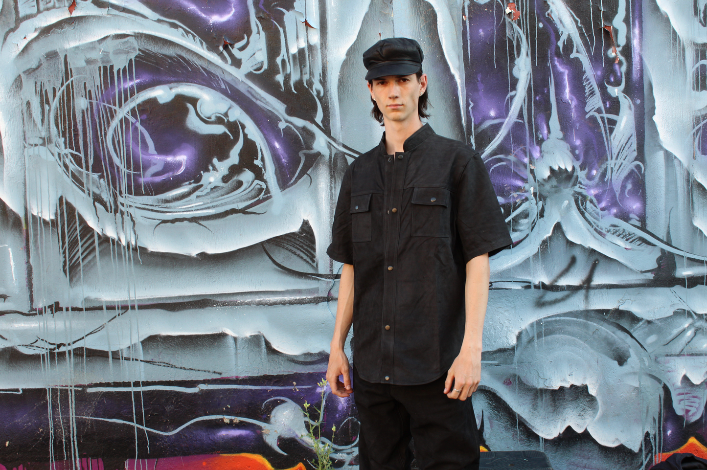 Person wearing a custom black leather outfit standing in front of a colorful graffiti wall.