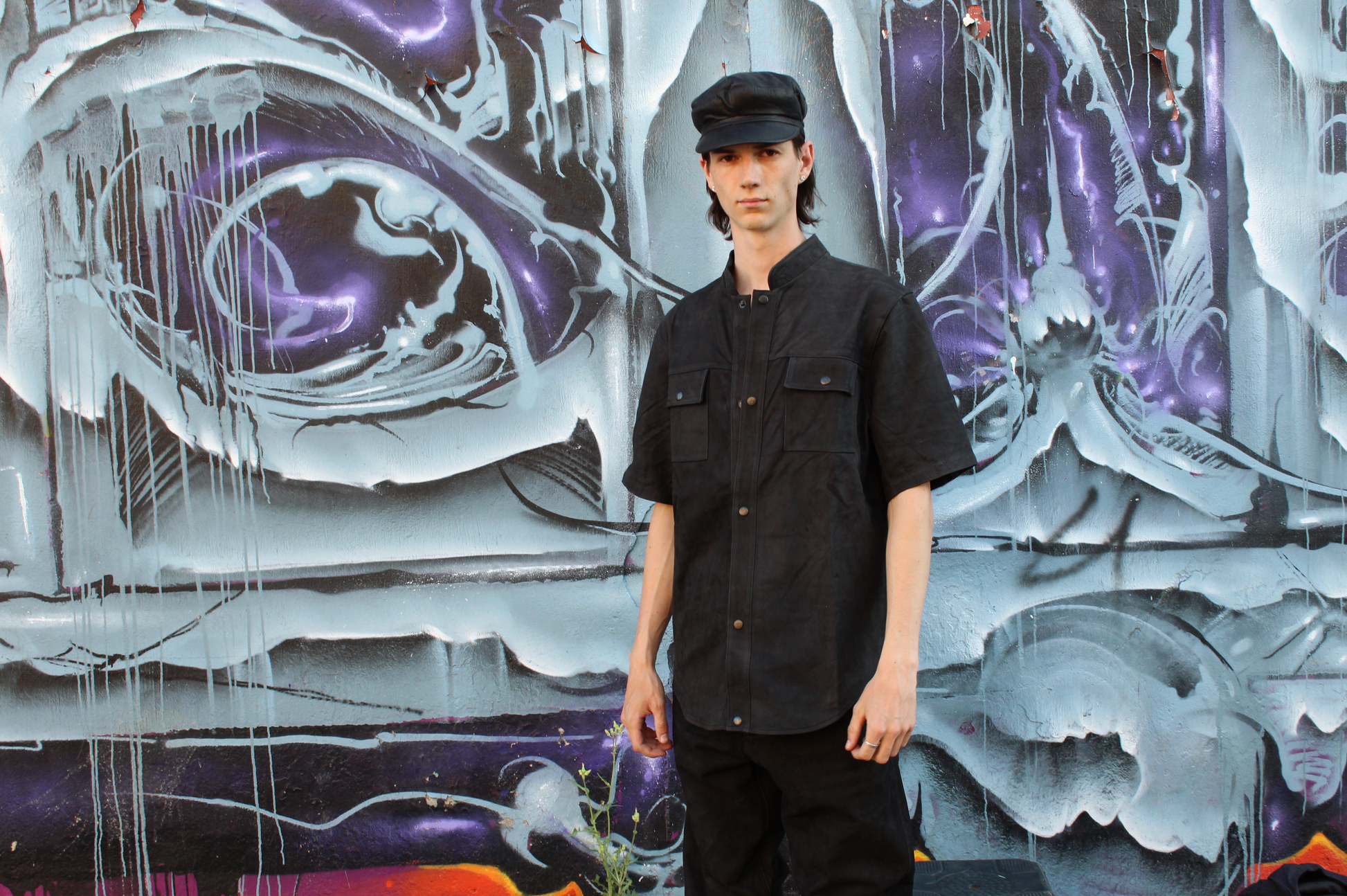 Person wearing a custom black leather outfit standing in front of a colorful graffiti wall.