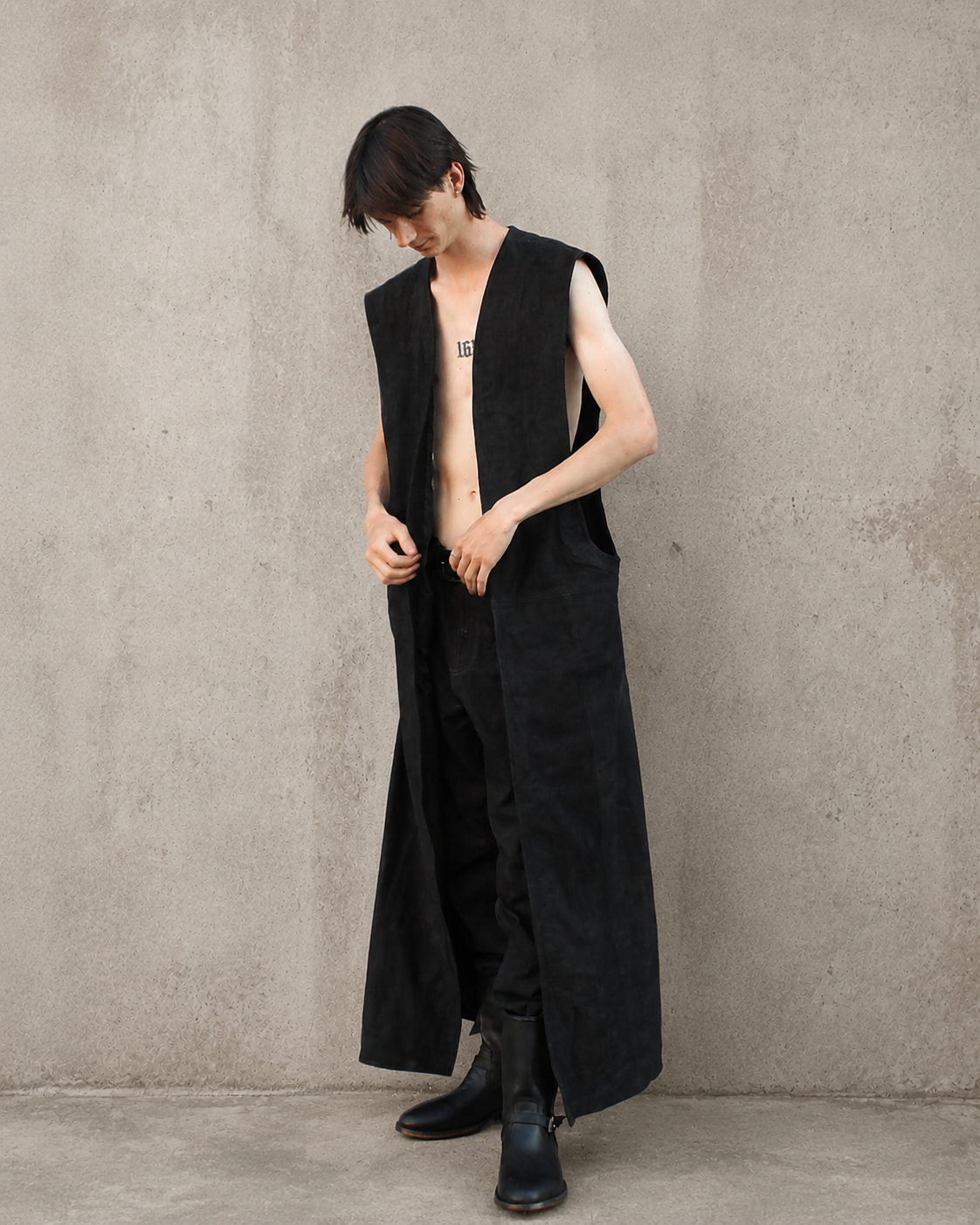 Tim wearing the Imminent Occurrence Sleeveless Duster against a warm cement background