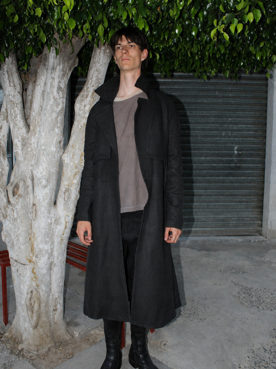 Model wearing the Imminent Occurrence handmade leather trench coat beneath a tree